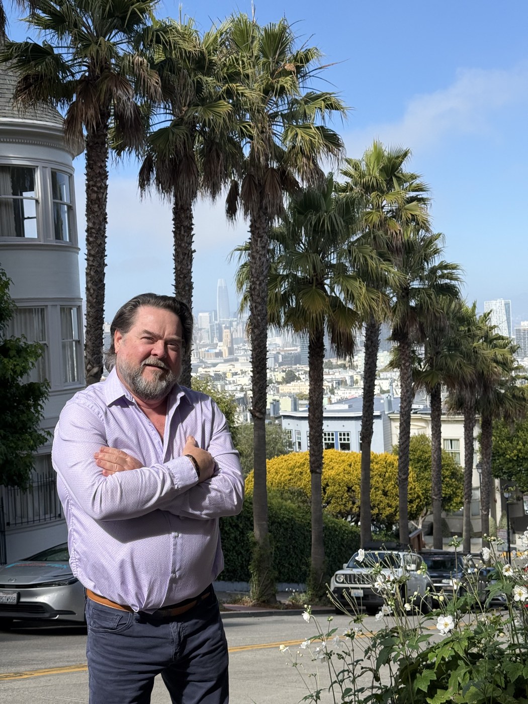 Eric Buckner standing on a palm-lined San Francisco street with the city skyline behind him